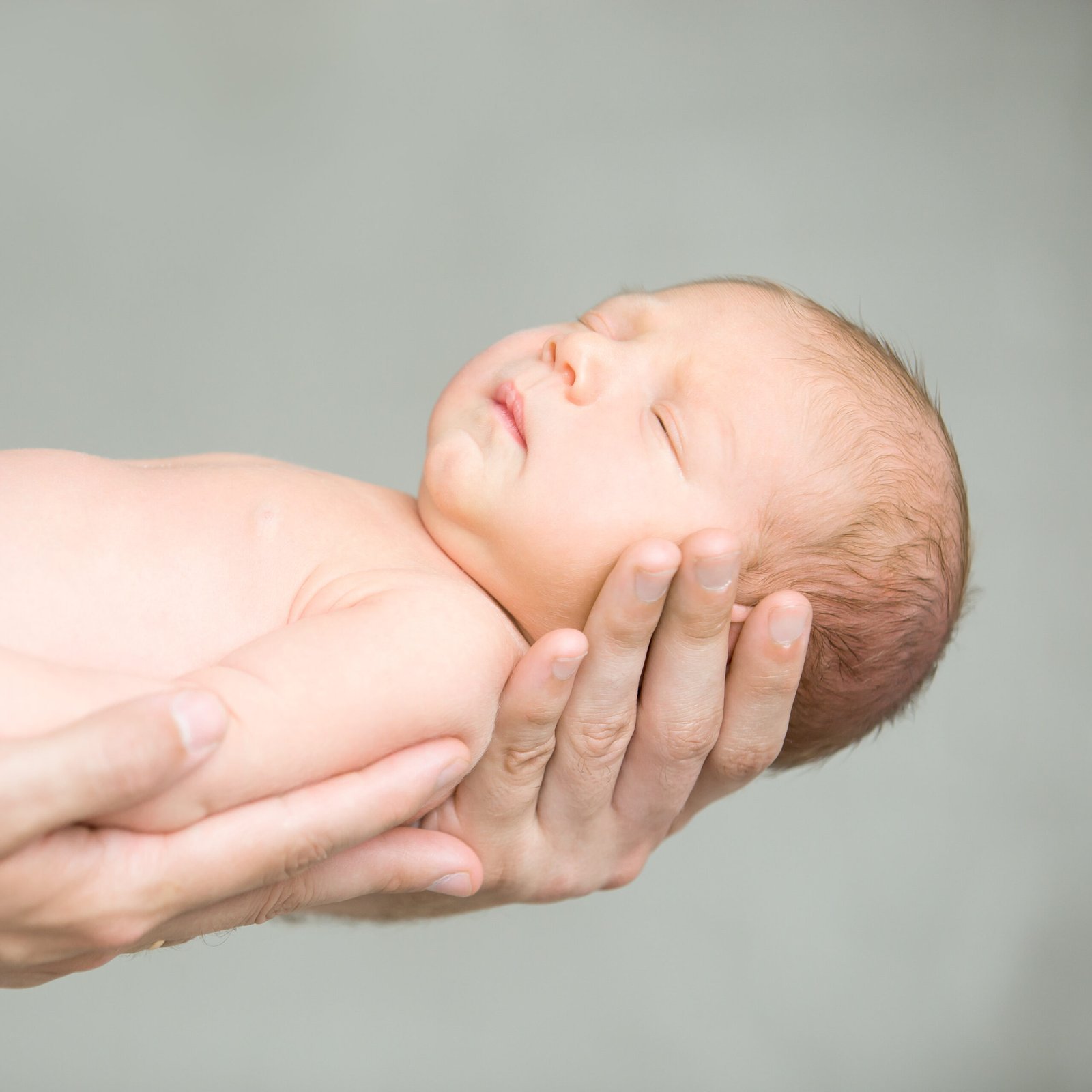 A sleeping newborn holding an adult's finger